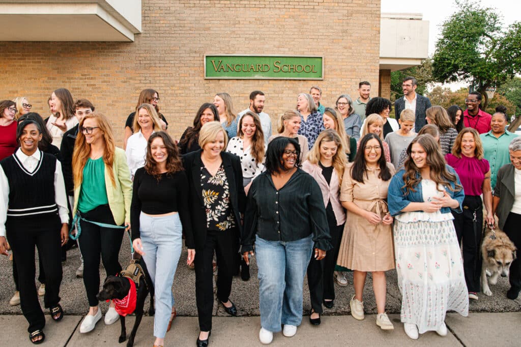 Vanguard School staff members posing together outside the school building, smiling and talking.